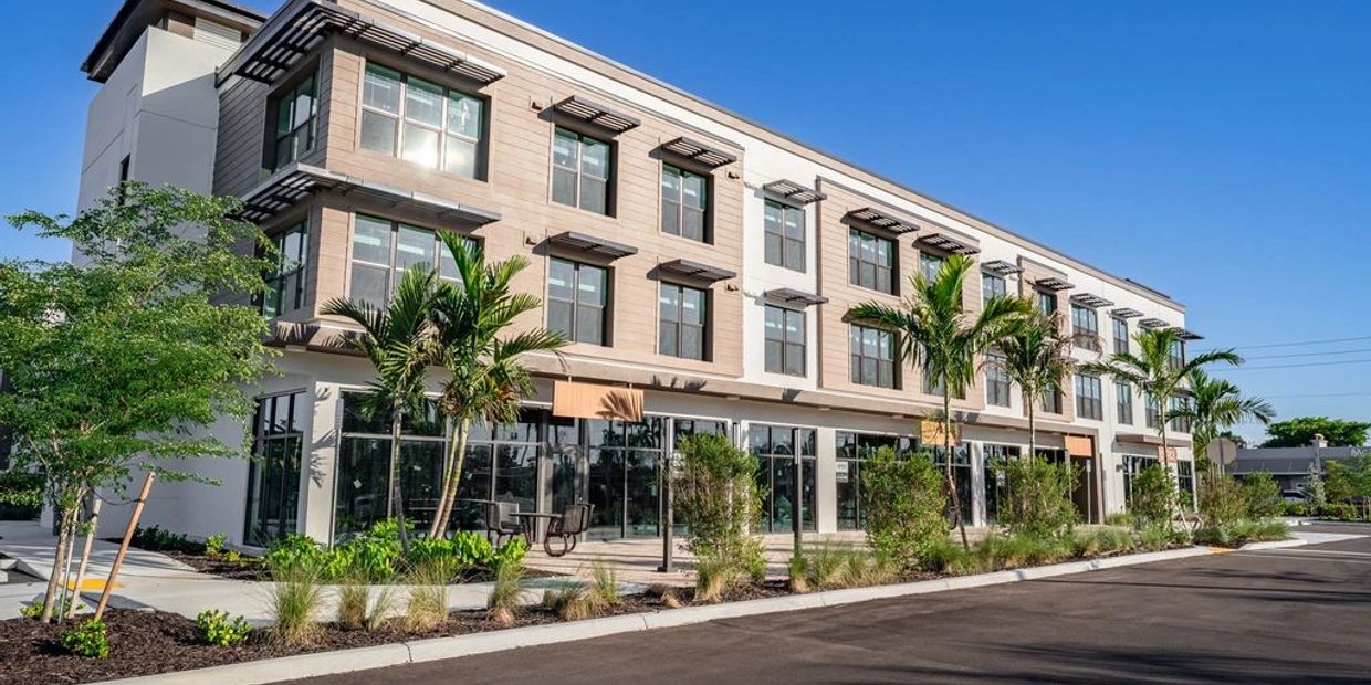 Modern three-story building with palm trees and blue sky.