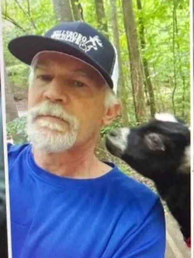 Man taking selfie with a goat in a forest.