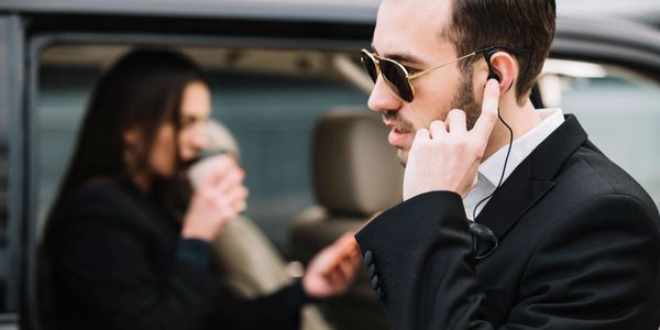 Security professional with earpiece conducting surveillance near a vehicle, illustrating discreet intelligence gathering.