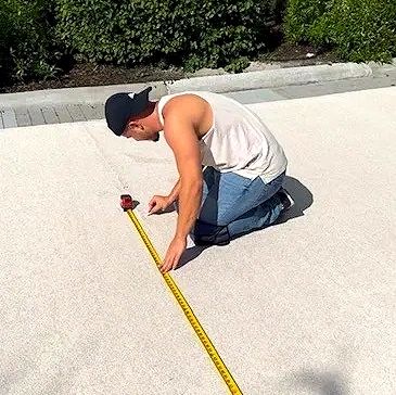 Man measuring distance on pavement with a tape measure.