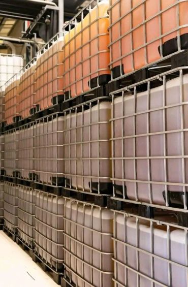 Rows of large industrial liquid containers stacked in a warehouse.