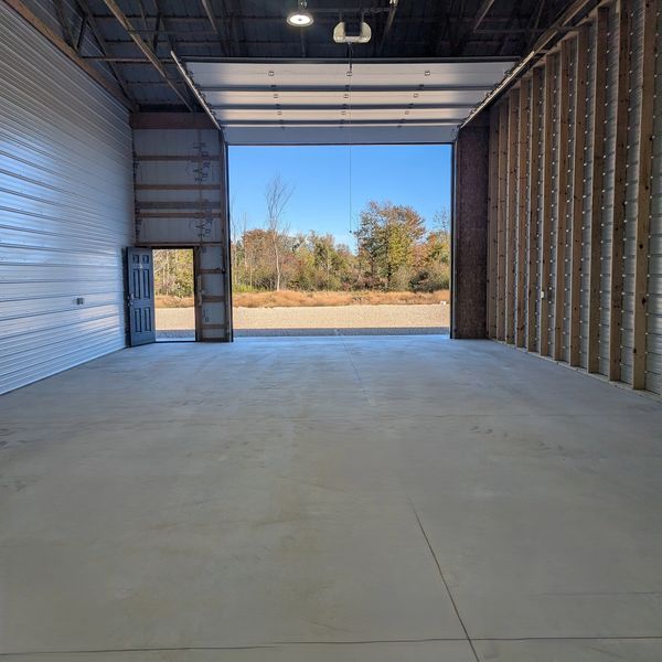 Empty garage with open door showing trees and blue sky.