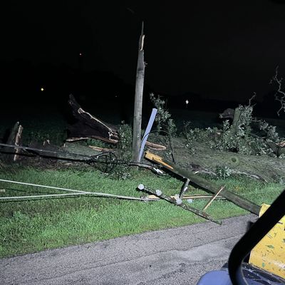 A broken utility pole lies on the ground at night, with wires scattered around.