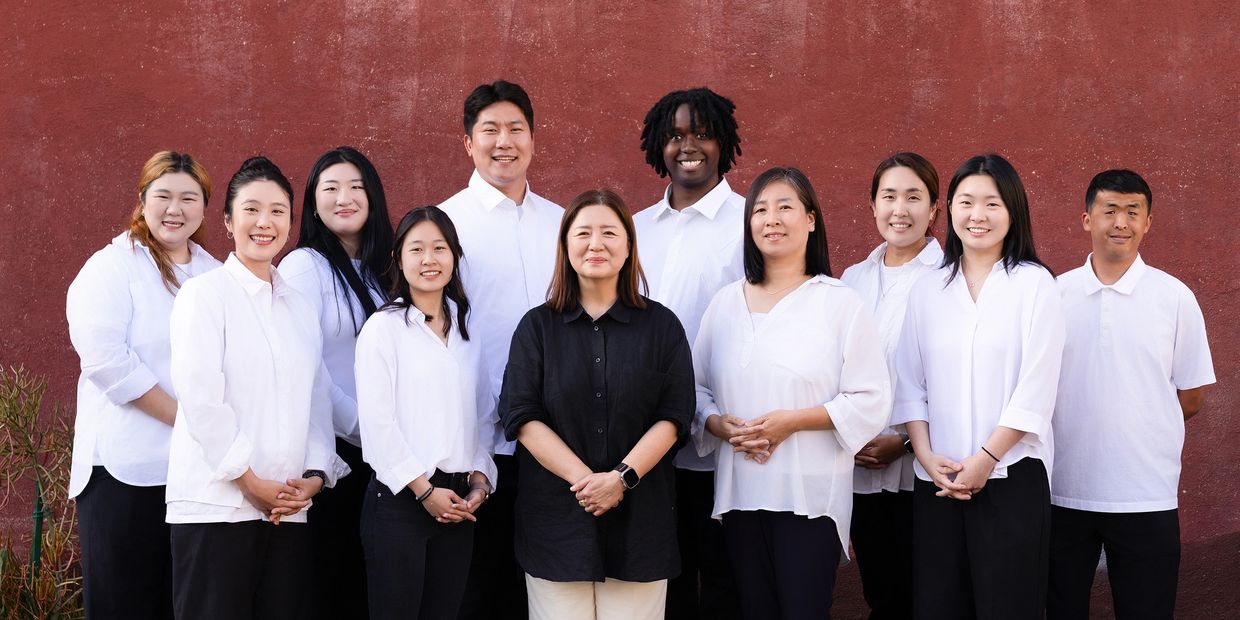 Group of diverse people smiling in white shirts against a red wall.