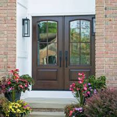 Double wooden front doors with glass panes and surrounding flowers.