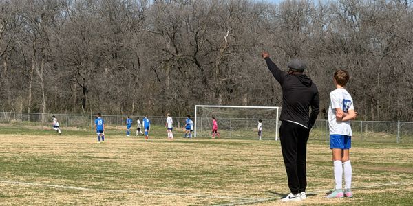 A soccer coach instructing young players on the field during a game.