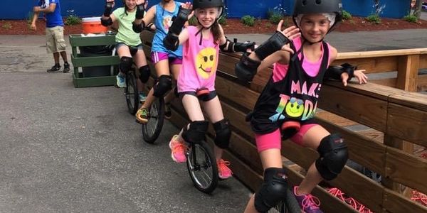 Group of kids riding unicycles outdoors with safety gear.