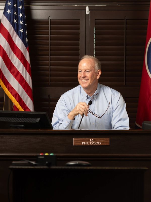 Phil Dodd smiling at his desk with flags behind him.