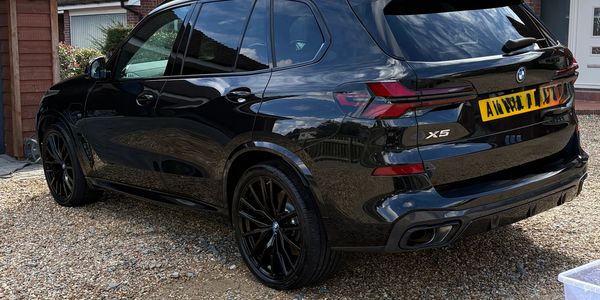 Sleek black BMW X5 parked on a gravel driveway beside houses.