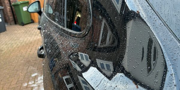 Reflection of houses on a wet black car surface with raindrops.