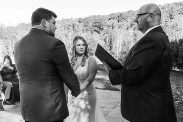 Couple holding hands during outdoor wedding ceremony with officiant.