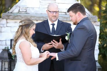 Couple exchanging rings during an outdoor wedding ceremony.