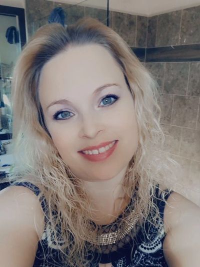 Smiling woman with curly blonde hair in a bathroom.