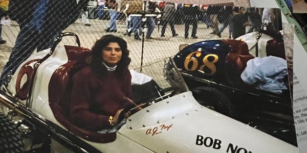 Woman sitting in a vintage race car labeled 'Bob Nowicke Fastener Special'.