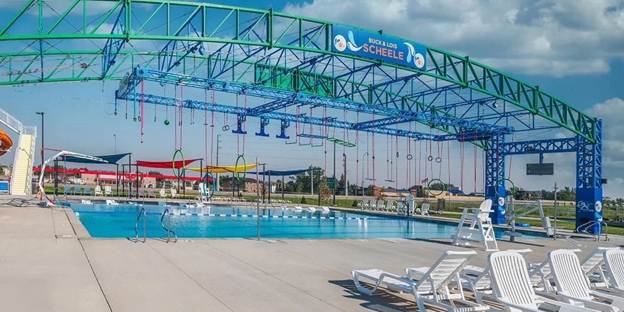 Outdoor swimming pool with obstacle course structure and lounge chairs.