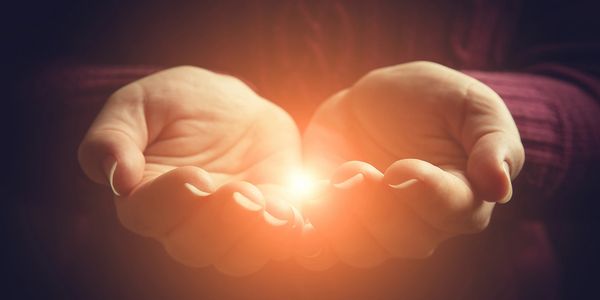 A man hand joins hands and a light appears from within.