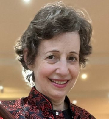 Smiling woman with curly hair in a patterned red and black jacket.
