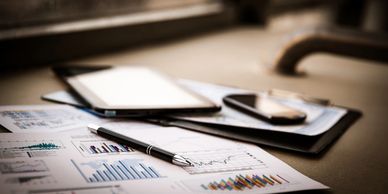 Desk with charts, a pen, tablet, and smartphone in soft focus.