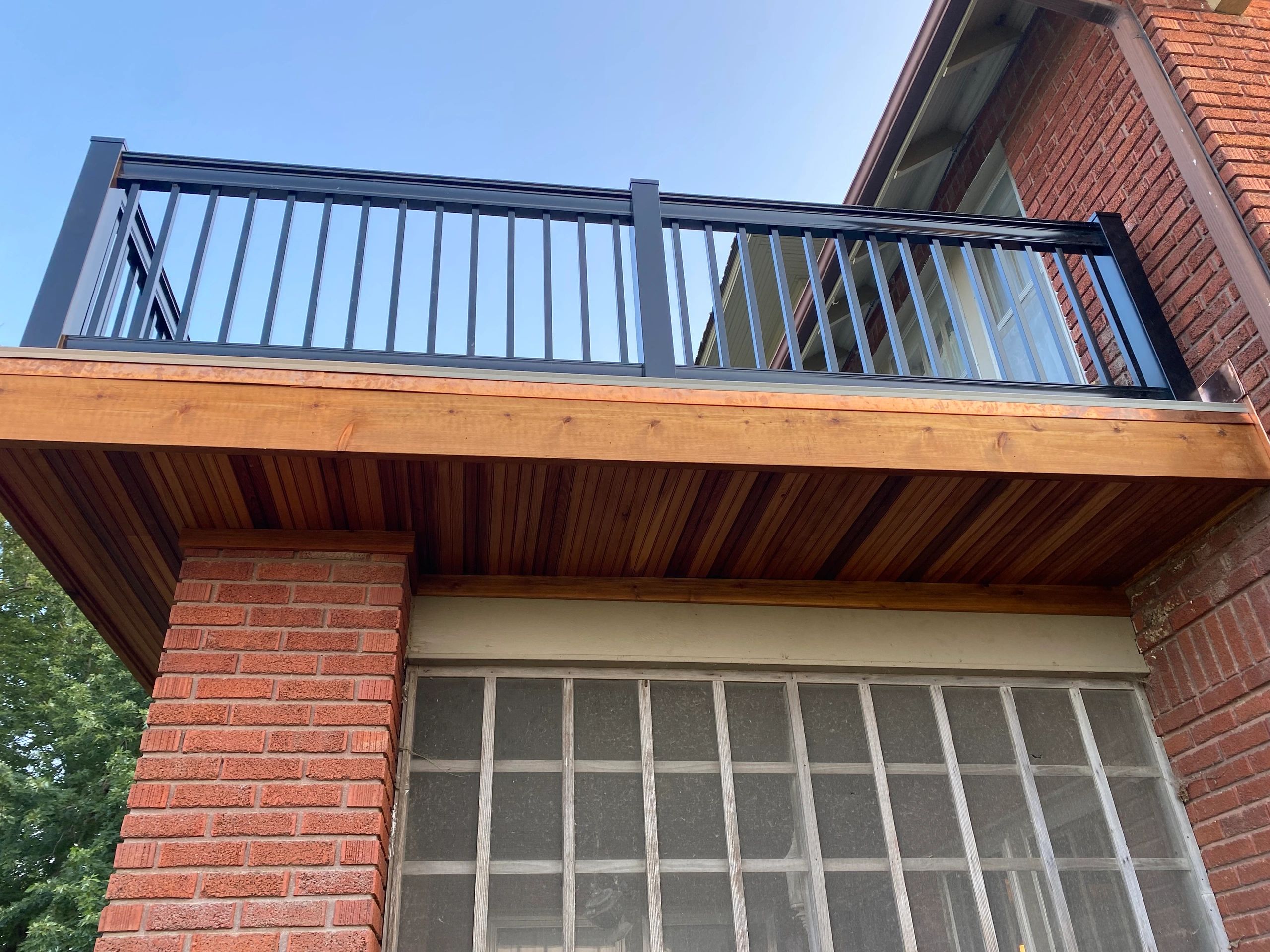 Black metal railing on a wooden balcony attached to a brick building.