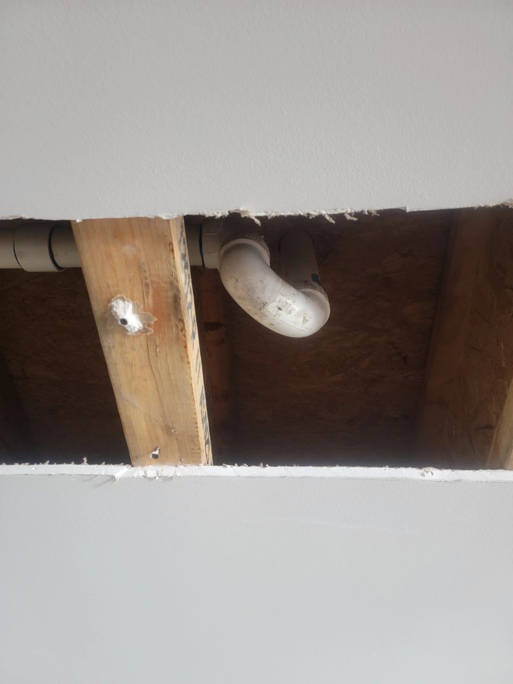Exposed ceiling with visible wooden beams and PVC pipe plumbing.
