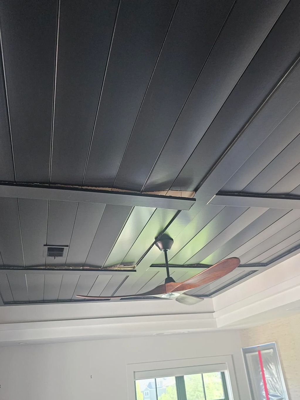 Ceiling with black panels and a wooden ceiling fan.