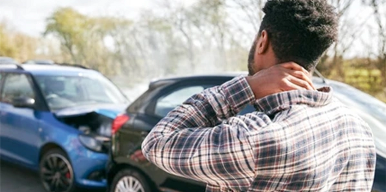 A Guy holding his neck while standing in front to two cars that were involved in an accident.