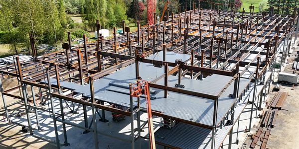 Steel framework of a large building under construction surrounded by greenery.