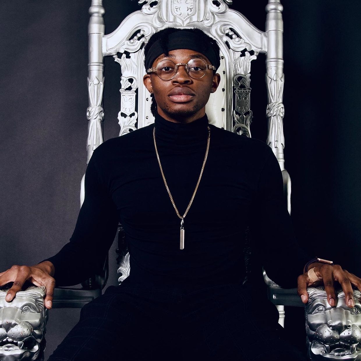 Man in black turtleneck sitting confidently on an ornate silver throne.