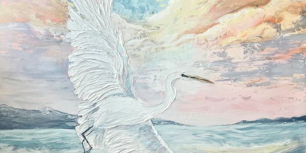 A white bird with spread wings flying over water at sunset.