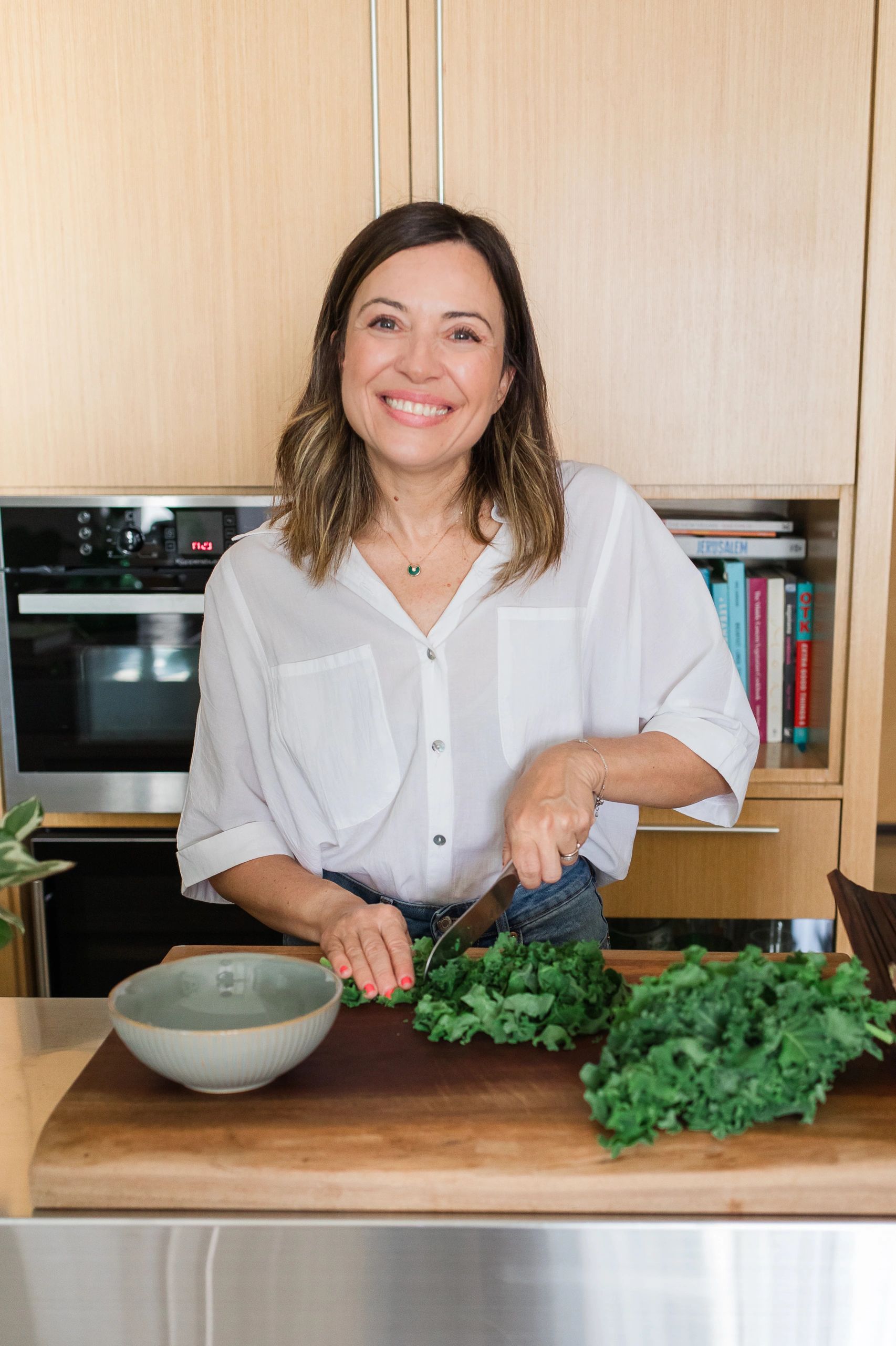 Smiling woman chopping fresh kale in a modern kitchen.