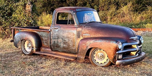 Old rusty pickup truck on grass near railway tracks.