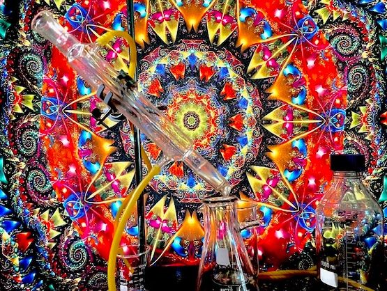 Colorful psychedelic backdrop with chemistry glassware setup in front.