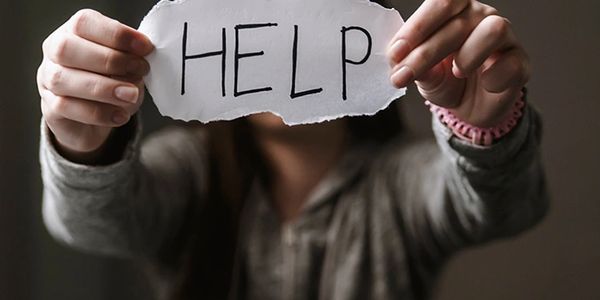 Woman holding up a paper with "HELP" written on it