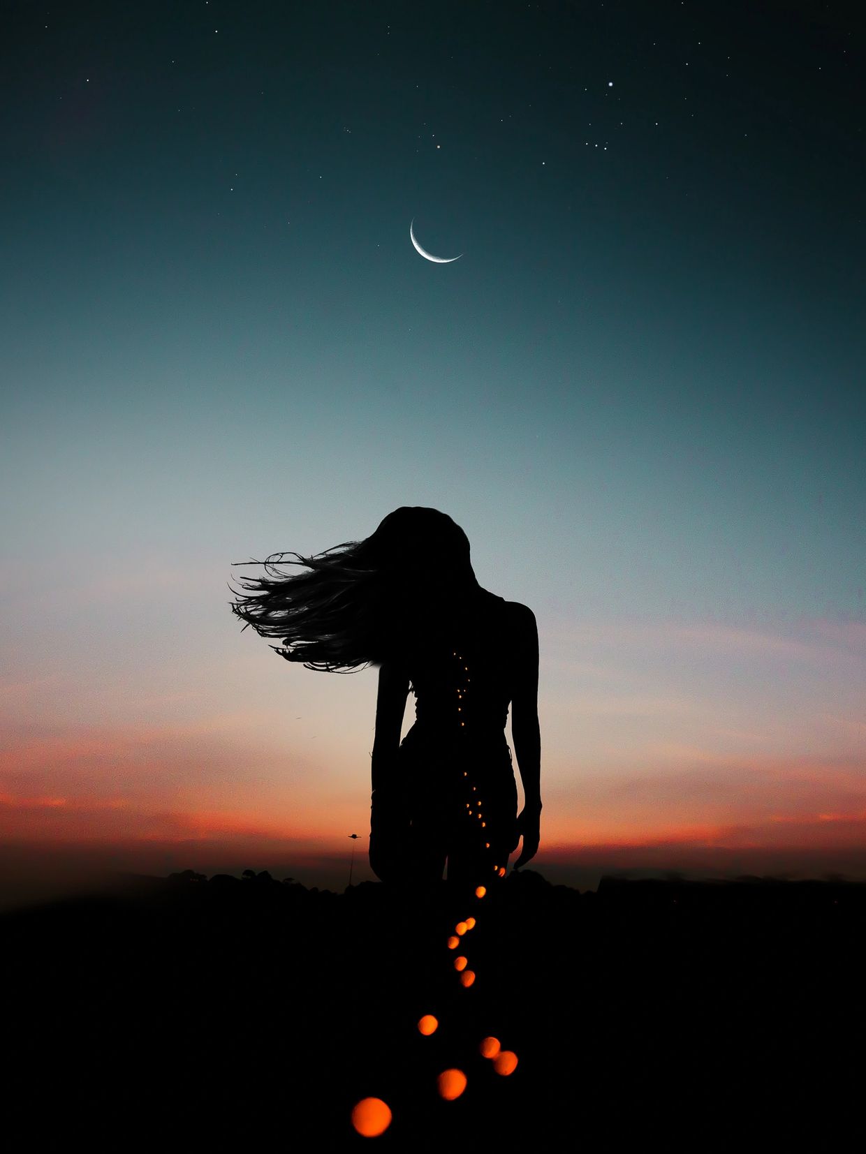 Silhouette of a woman with her hair blowing in the wind against the night sky with the crescent moon
