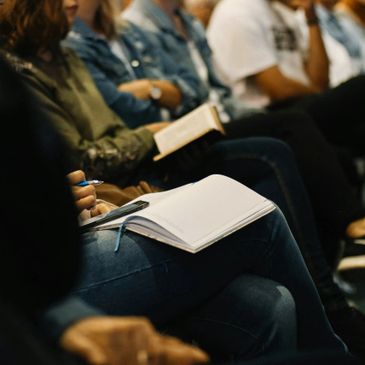 People seated, taking notes and reading books during a session.