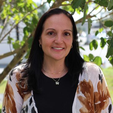 Woman posing outdoors with greenery in the background.