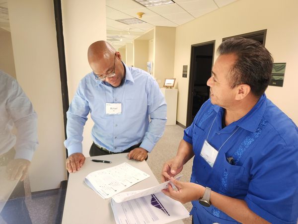 Two men in a discussion over documents, wearing name tags at a professional setting.