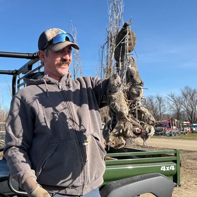 Man holding a bundle of harvested root vegetables outdoors.