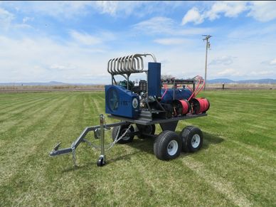 A blue mechanical device on a four-wheeled trailer on a grassy field.
