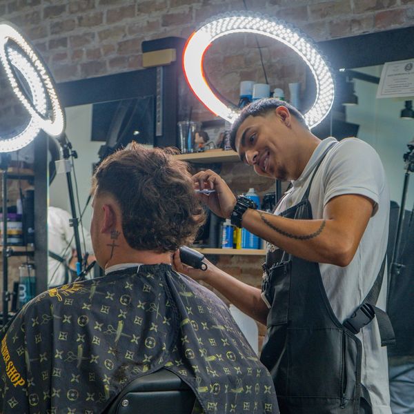 Barber giving a haircut in a well-lit salon with a ring light.
