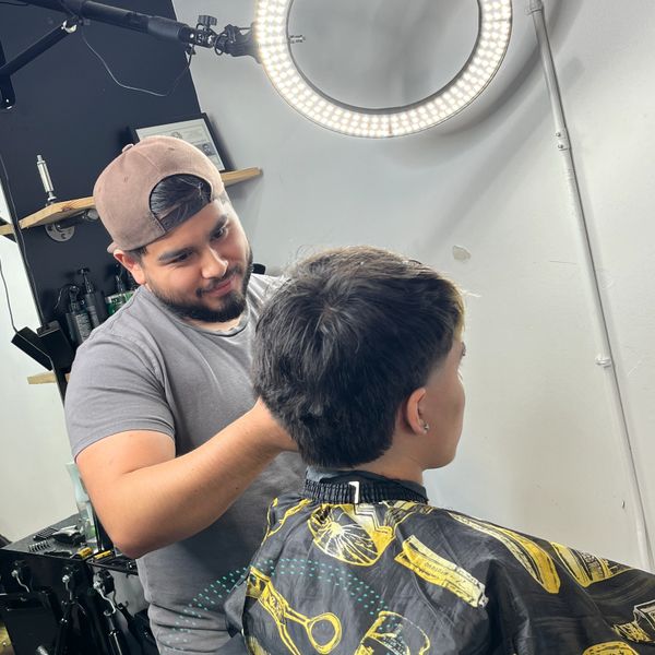 Barber giving a haircut to a young client under a ring light.
