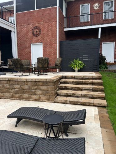 Outdoor patio with chairs, loungers, and stairs leading to a brick house.
