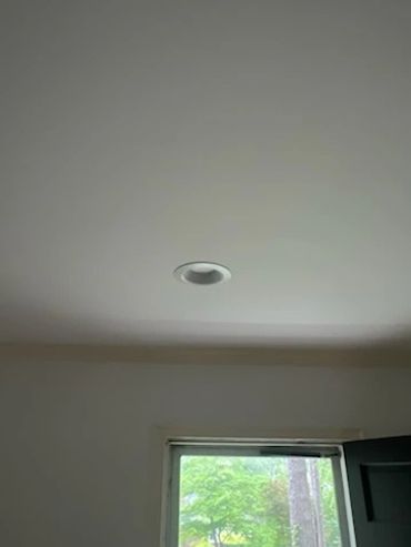 Ceiling with a recessed light fixture above a window showing green trees outside.