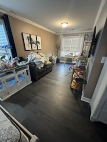 Living room with dark flooring, black couch, and cluttered surfaces under soft lighting.