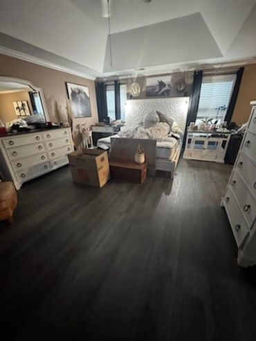 Cozy bedroom with white furniture and dark flooring, featuring a bed and packed boxes.