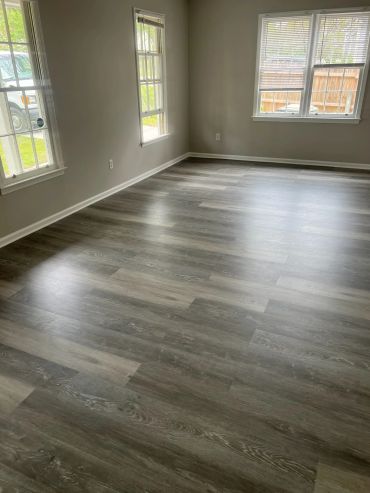 Empty room with gray wood flooring and natural light from windows.