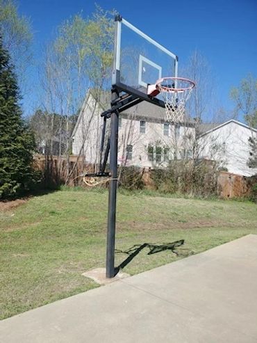 A basketball hoop standing on a concrete driveway with houses and trees in the background.