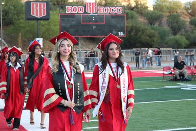 Two female graduates in red gowns walking on a football field.