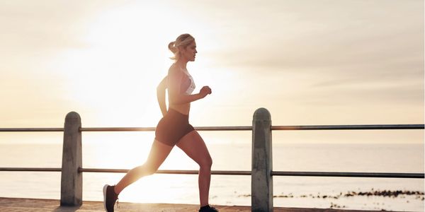 A woman running outdoors by the waterfront during sunrise.
