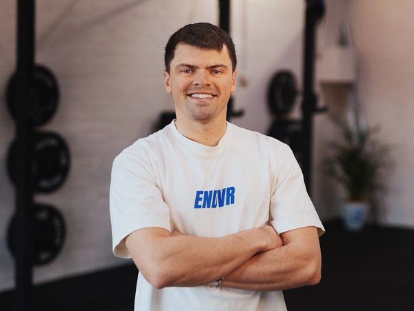 Man in white T-shirt smiling with arms crossed.